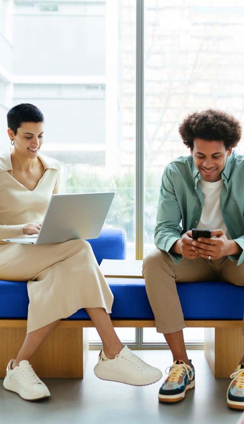 two people sitting on a bench with devices