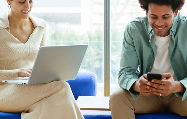 two people sitting on a bench with devices