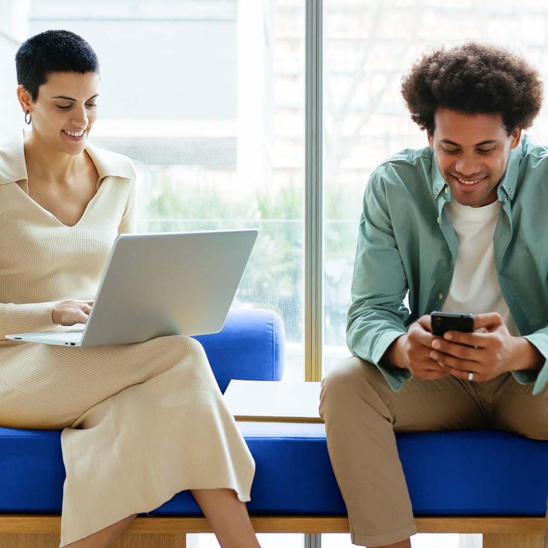 two people sitting on a bench with devices